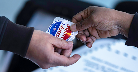 Two hands holding an I voted sticker 