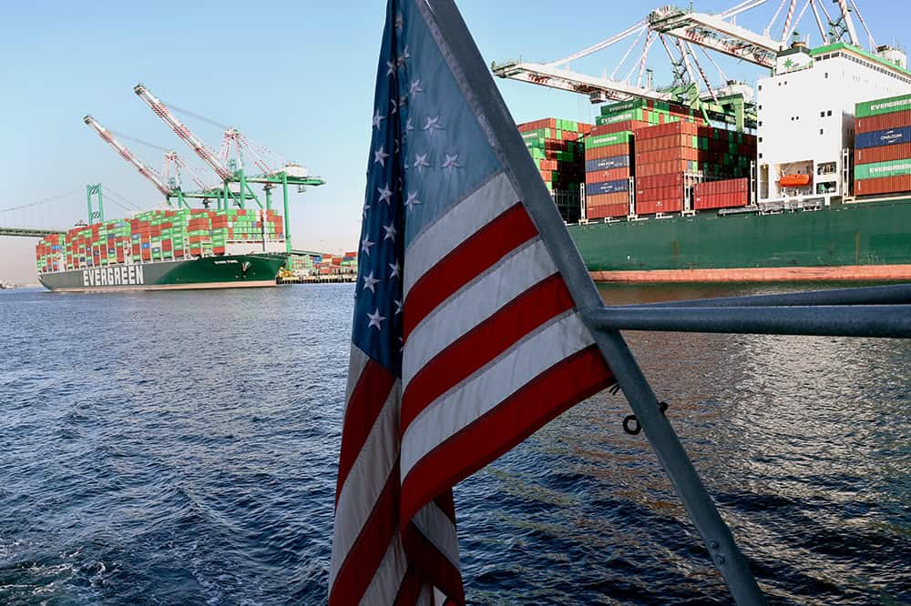 An American flag flies from a ferry passing container ships