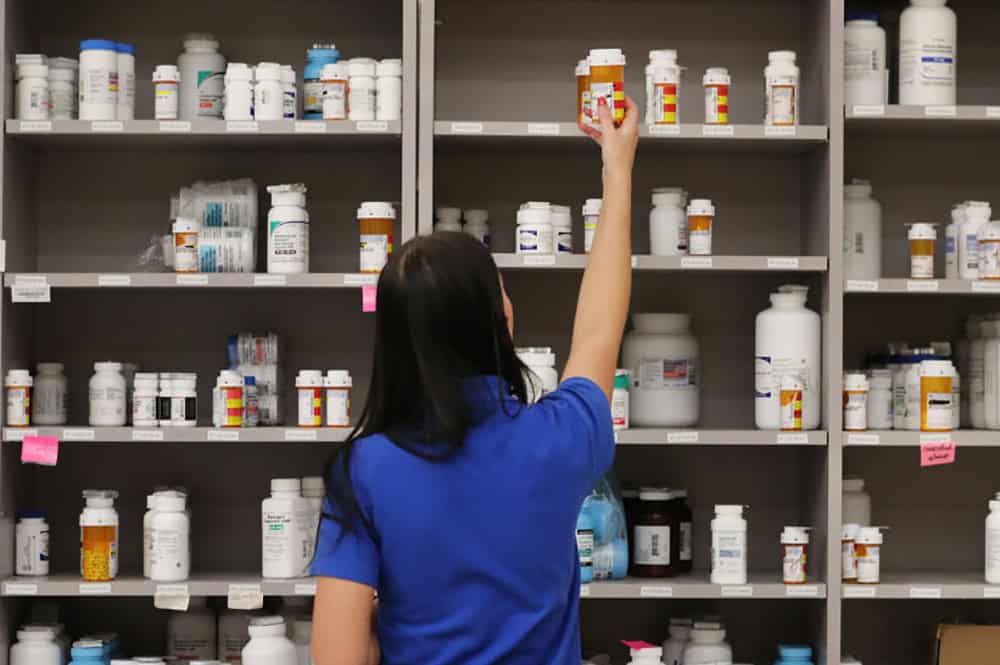 A pharmacy technician grabs a bottle of drugs off a shelve