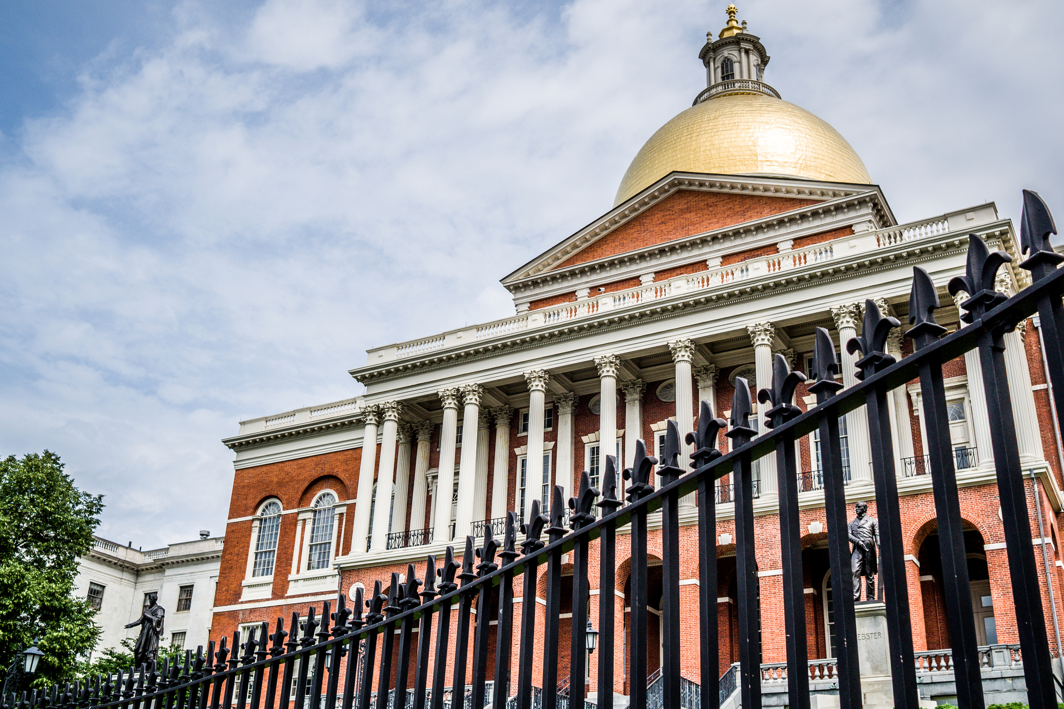 The Massachusetts State House stands behind an iron fence in Boston, MA.