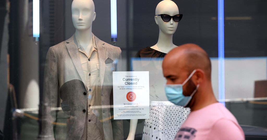 Man in a mask walking in front of a closed storefront